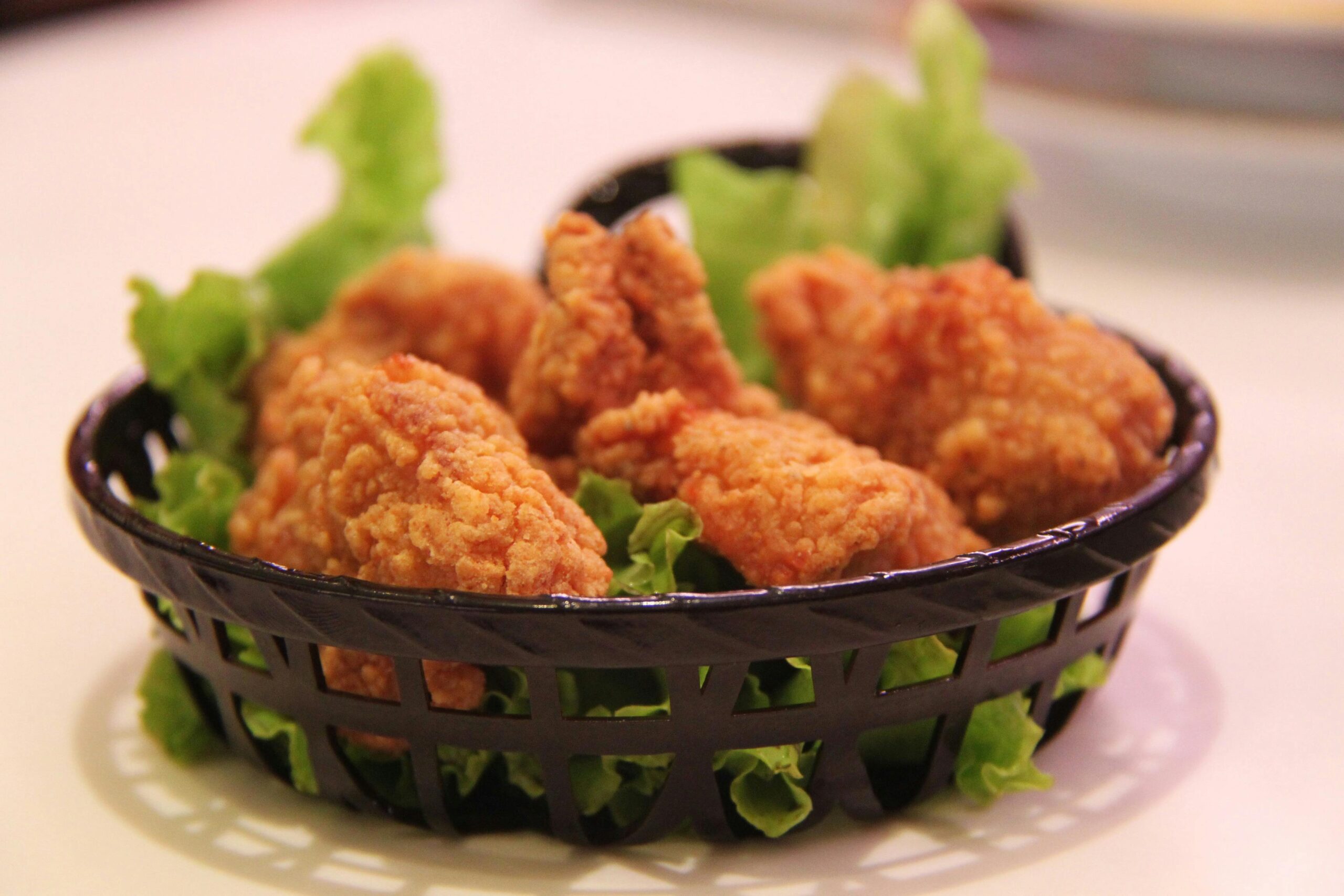 Close-up of crispy fried chicken served in a black basket with fresh lettuce, highlighting food texture.