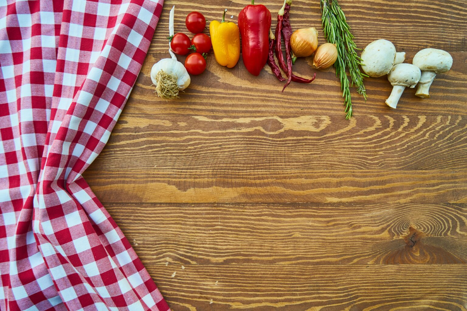 Fresh vegetables and spices on a rustic wooden table with checkered cloth.